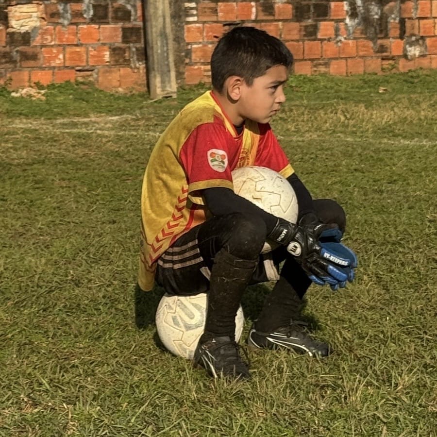 Young boy goalkeeper sitting on a field with NYK kids goalkeeper gloves, ready for training
